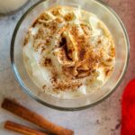 eggnog with whipped cream and cinnamon next to two cinnamon sticks