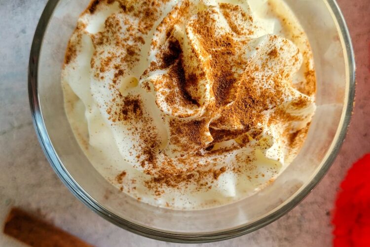 eggnog with whipped cream and cinnamon next to two cinnamon sticks