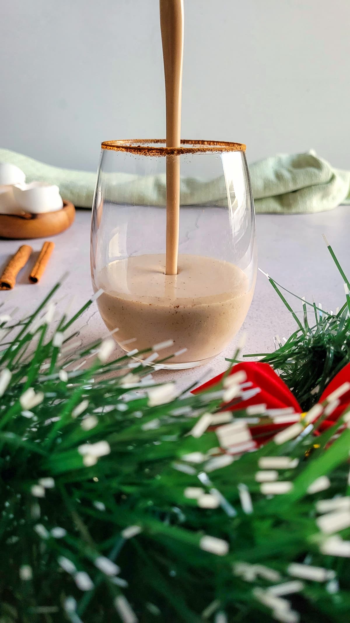 eggnog being poured into a cinnamon rimmed glass