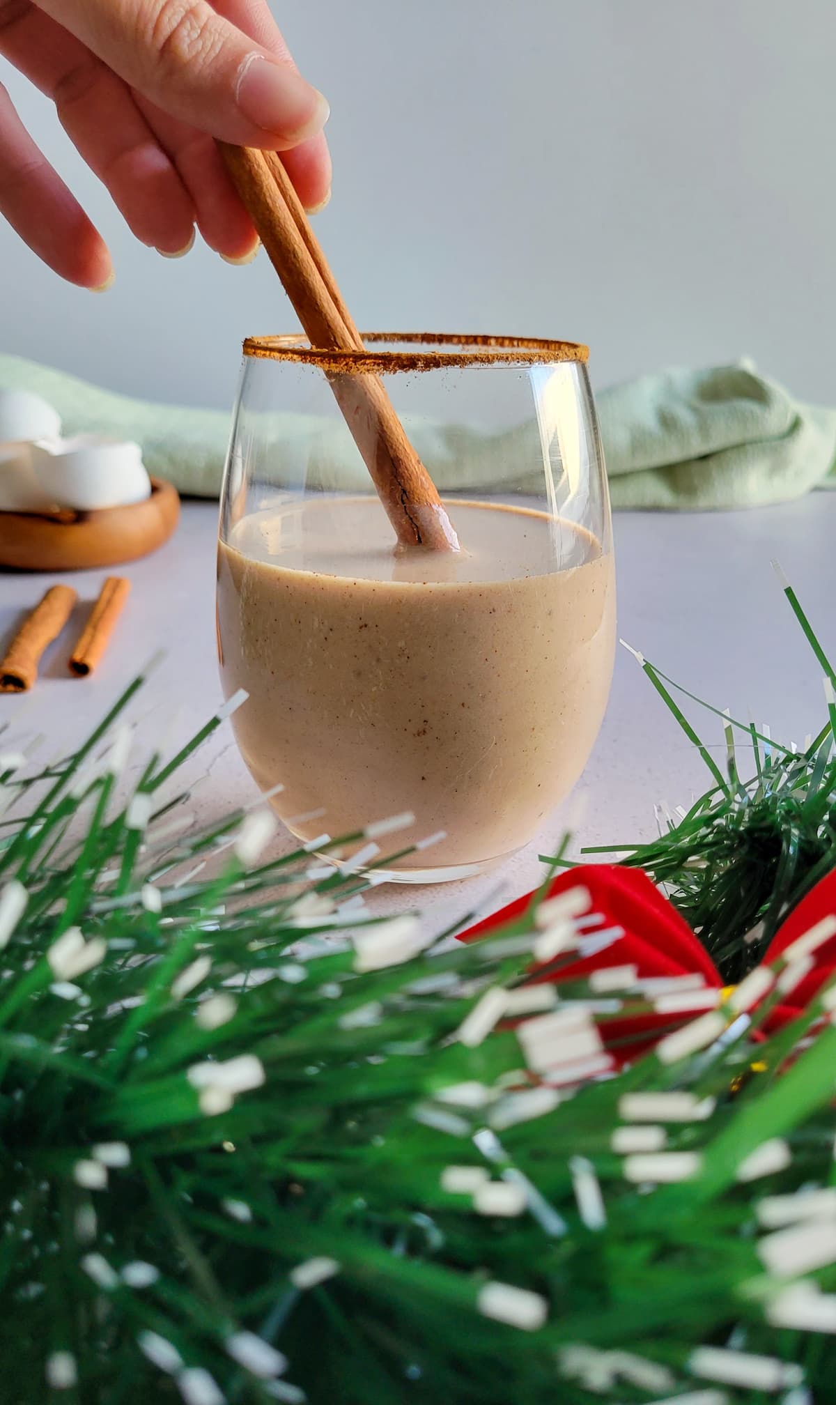 hand touching a cinnamon stick in a glass of eggnog