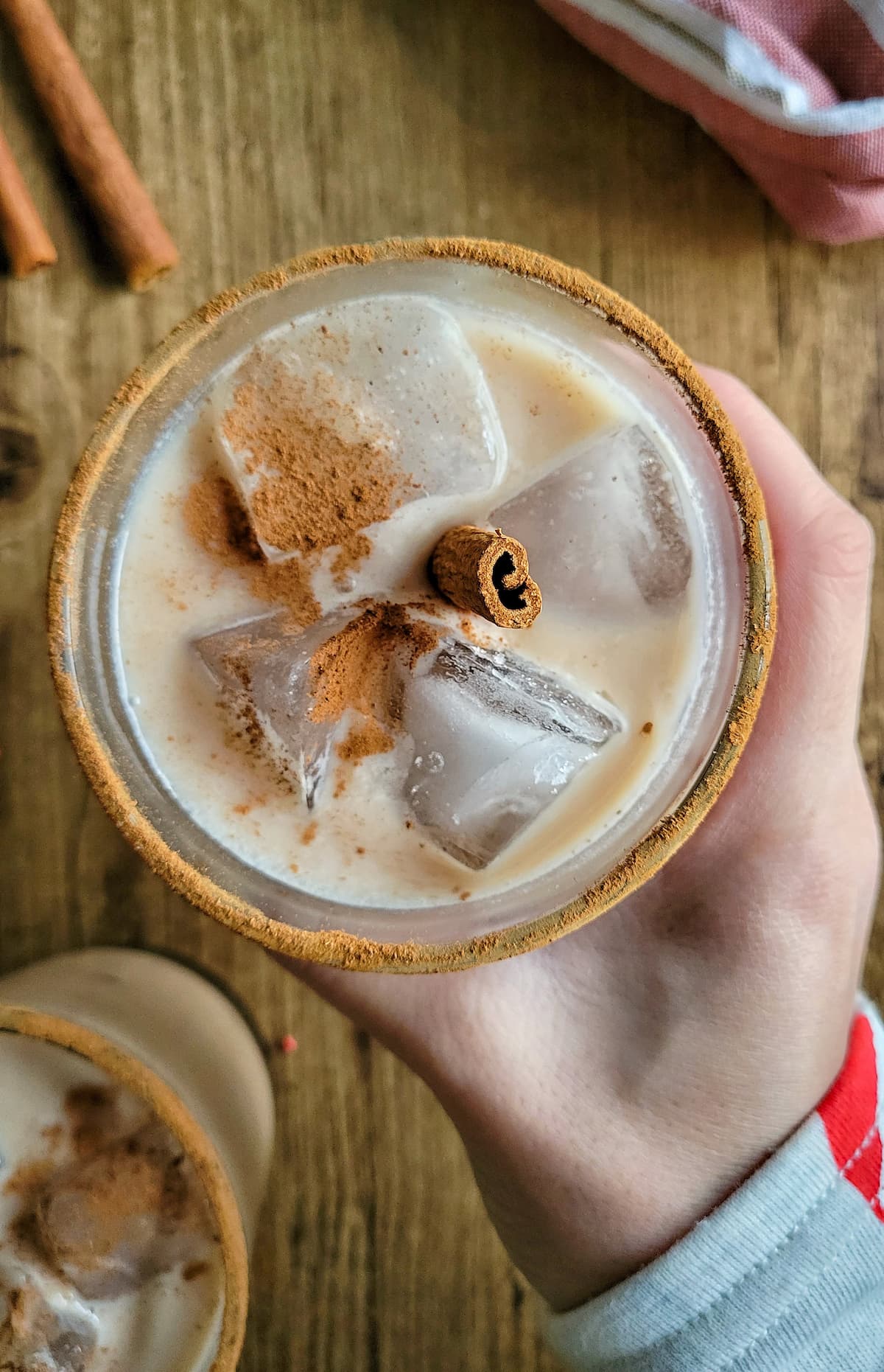 hand holding a rum and eggnog garnished with cinnamon and cinnamon stick