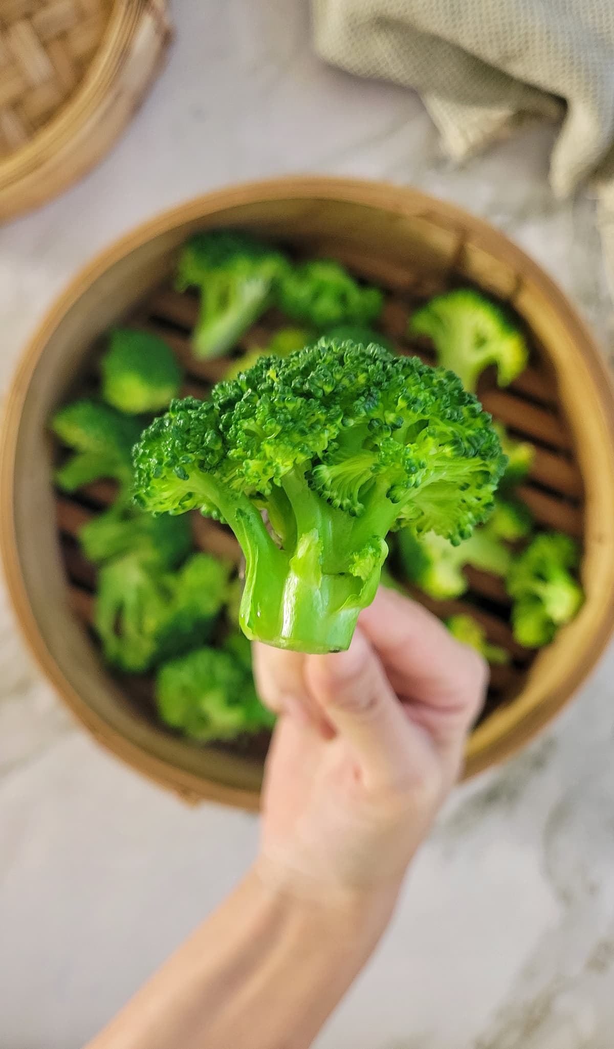 fork holding up a broccoli floret over a steamer basket with more