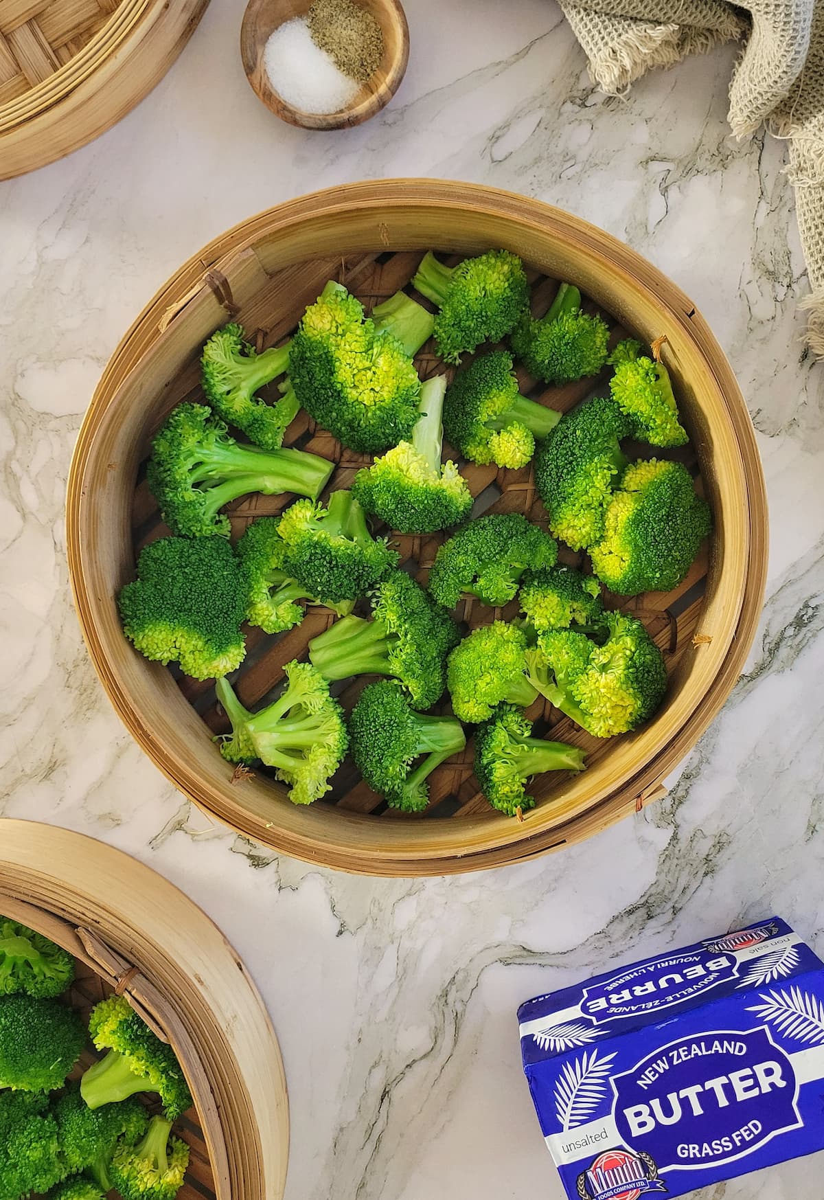 broccoli florets in a bamboo steamer basket, brick of butter and salt and pepper in the background