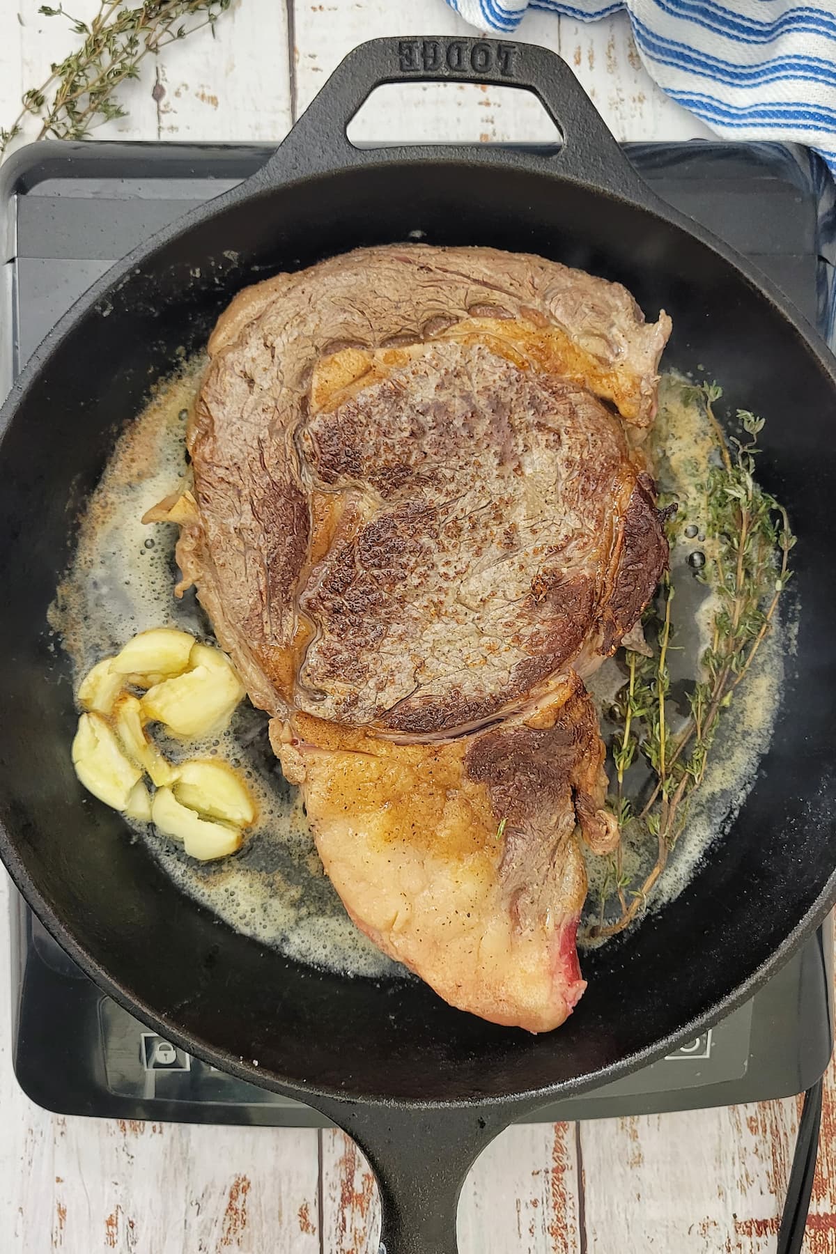 ribeye steak cooking in a cast iron skillet with butter, garlic and fresh thyme