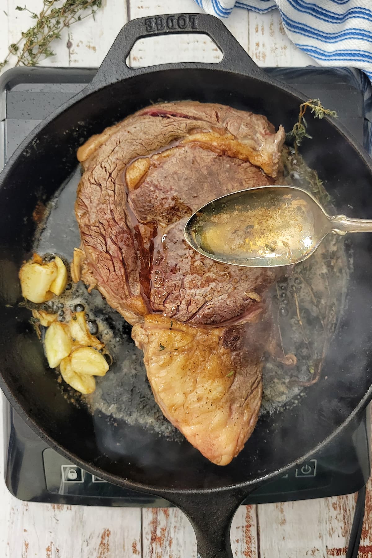 spoonful of butter over a ribeye steak in a cast iron skillet with garlic