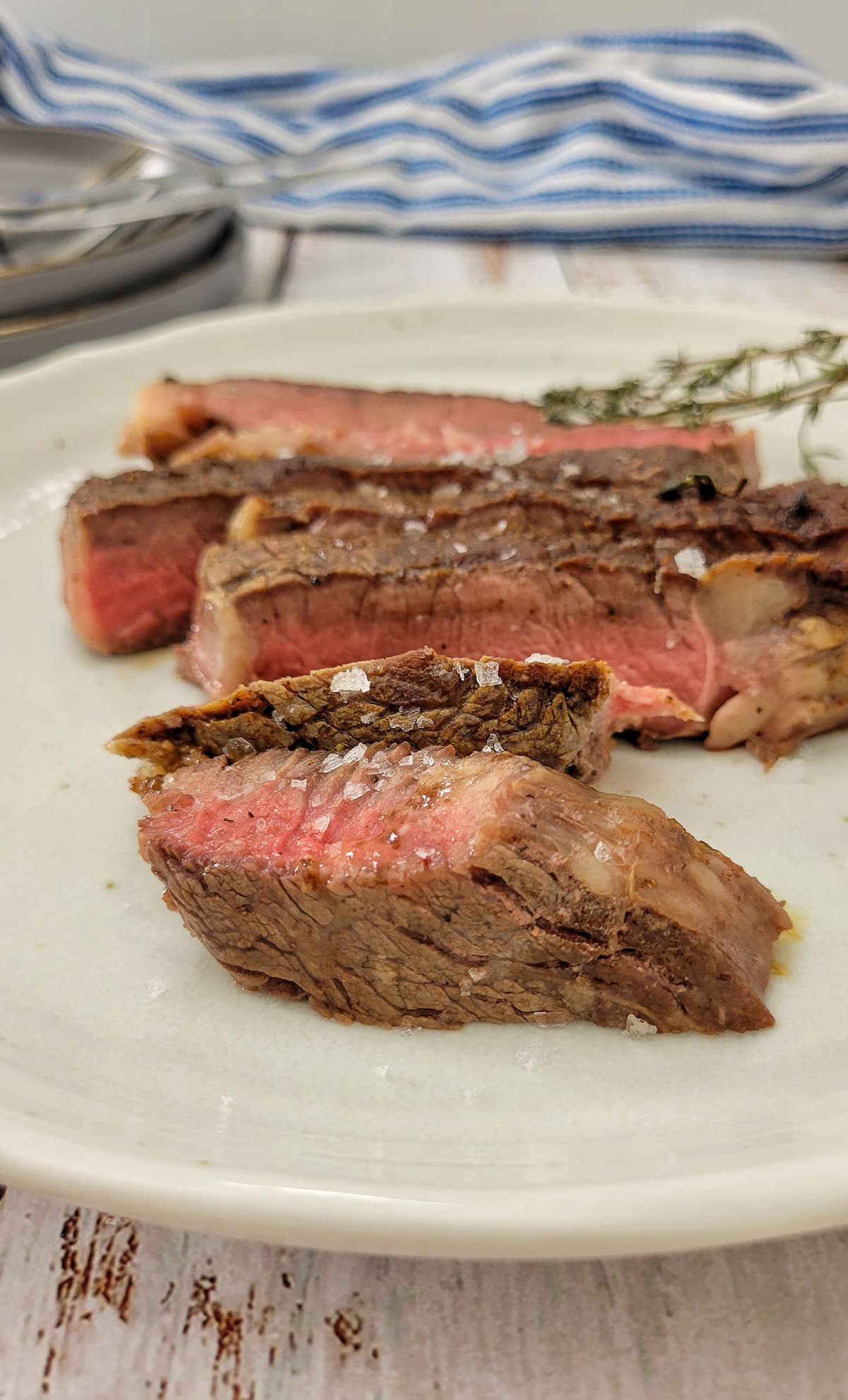 sliced medium rare ribeye steak with maldon salt and fresh thyme in the background