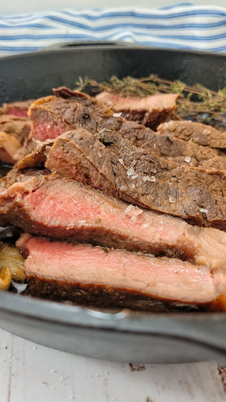 slices of medium rare steak in a cast iron skillet with maldon sea salt, fresh thyme in the background