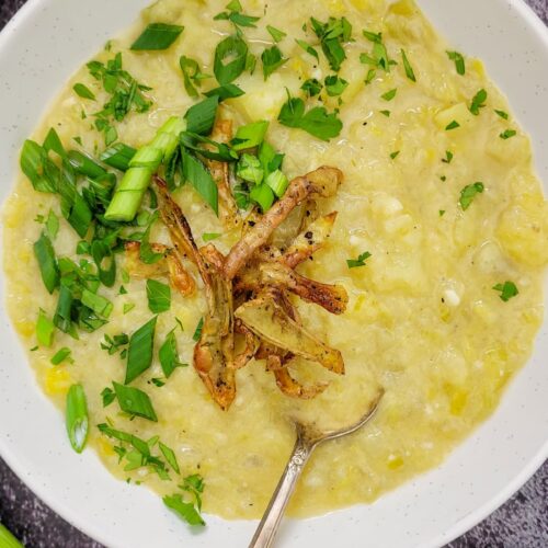 bowl of creamy yellow soup with chopped green onions, parsley and potato peels
