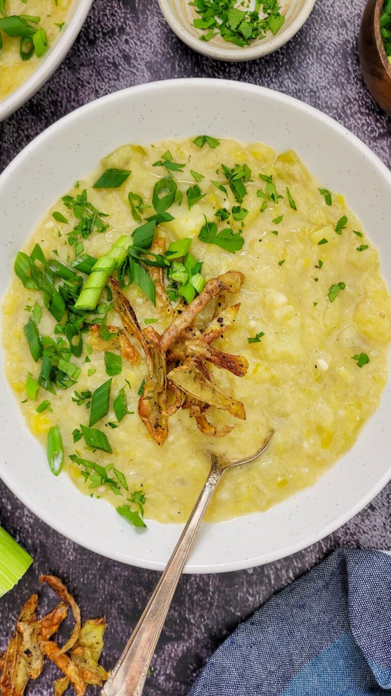 bowl of creamy yellow soup with chopped green onions, parsley and potato peels