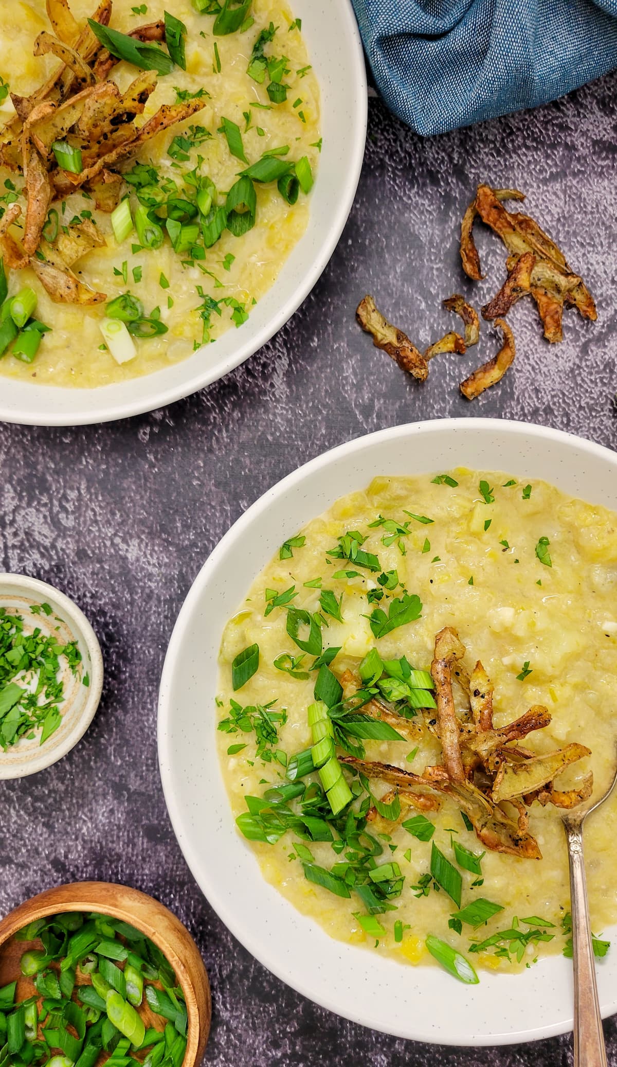 two bowls of potato leek soup with chopped green onions, parsley and crispy potato peels