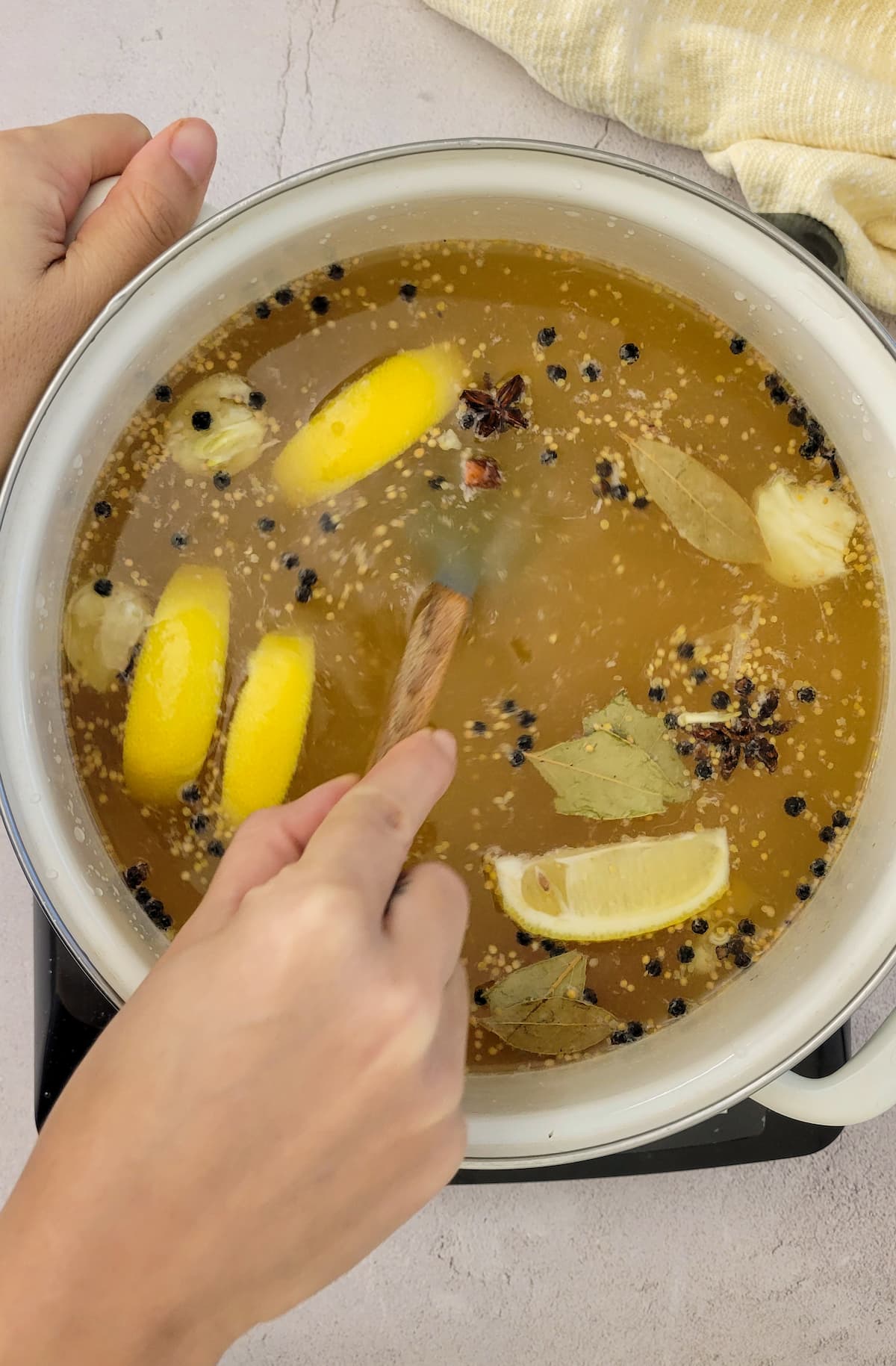 hand stirring liquid in a pot with peppercorns, lemon wedges and bay leaves