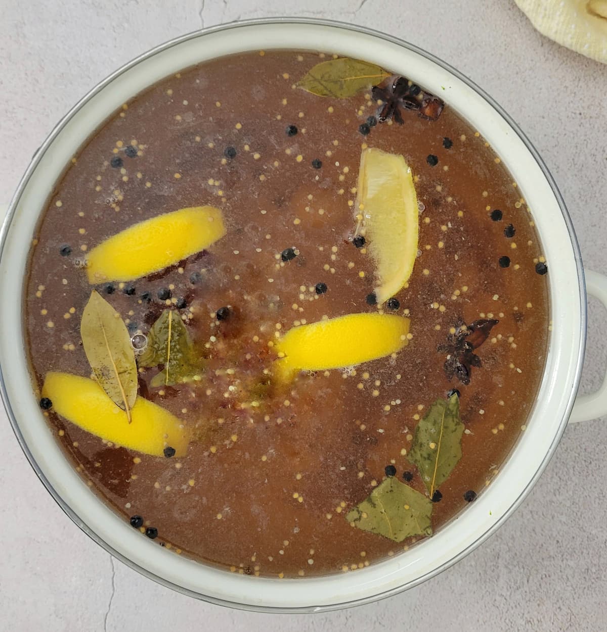liquid in a pot with lemon wedges, peppercorns, bay leaves and star anise