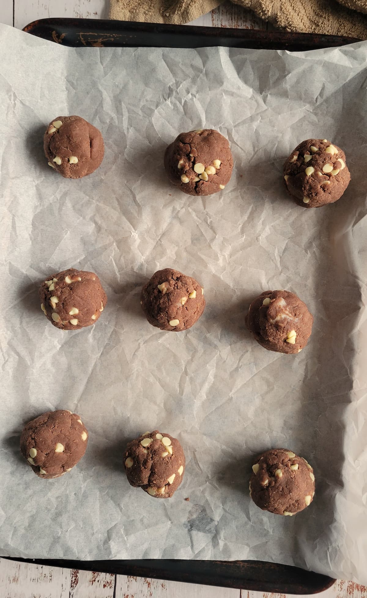 balls of chocolate dough with white chocolate chips laid out on a parchment lined baking sheet