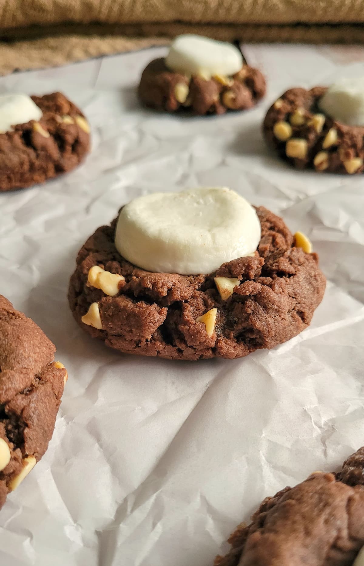 hot cocoa cookies with white chocolate chips and a giant marshmallow on a piece of parchment paper