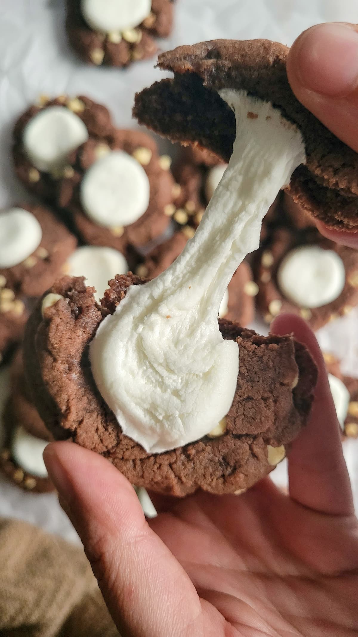 hand pulling apart a hot cocoa cookie to showcase a gooey marshmallow over a batch of the rest