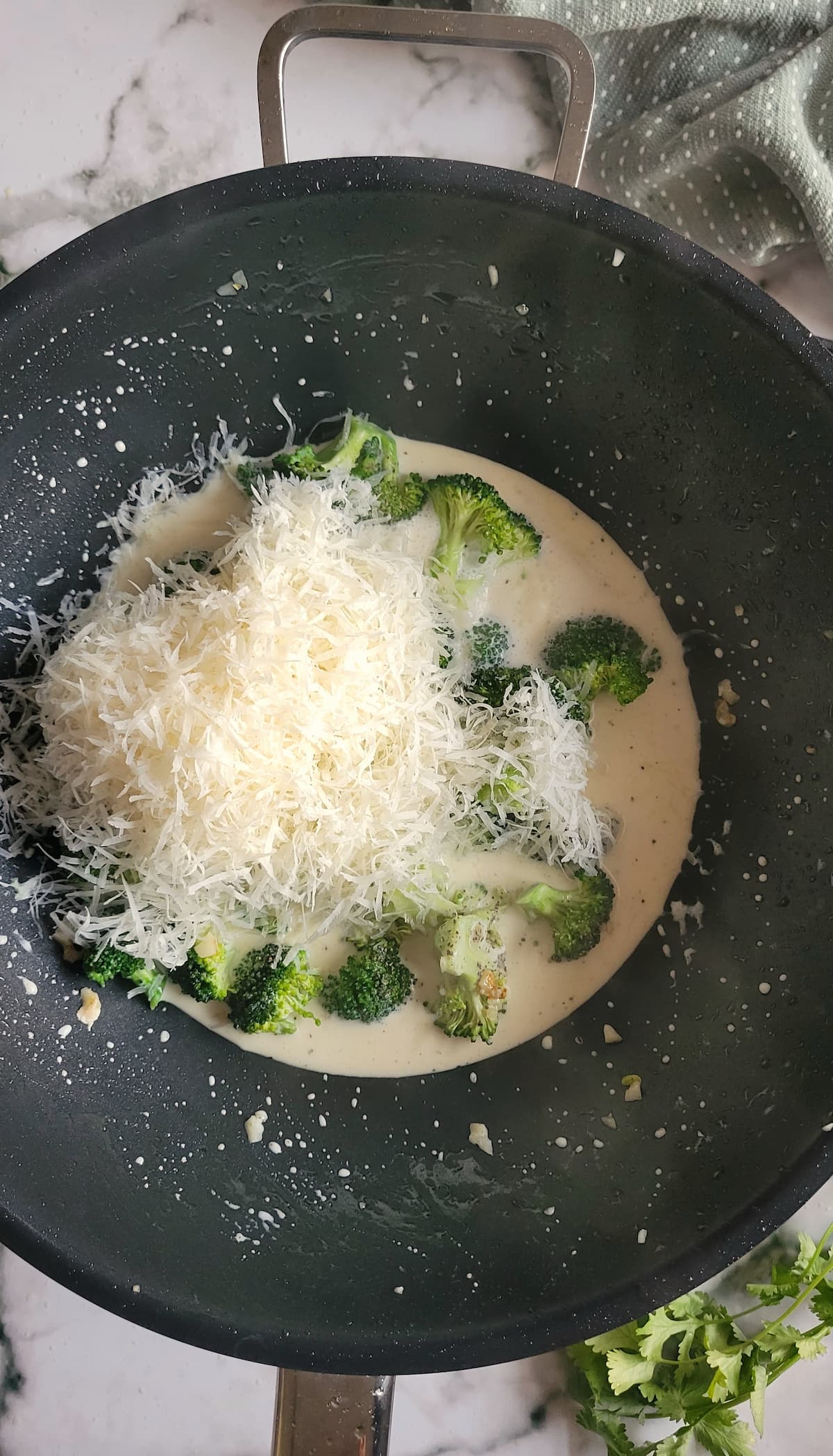 broccoli florets in a creamy sauce in a wok with shredded parmesan cheese on top