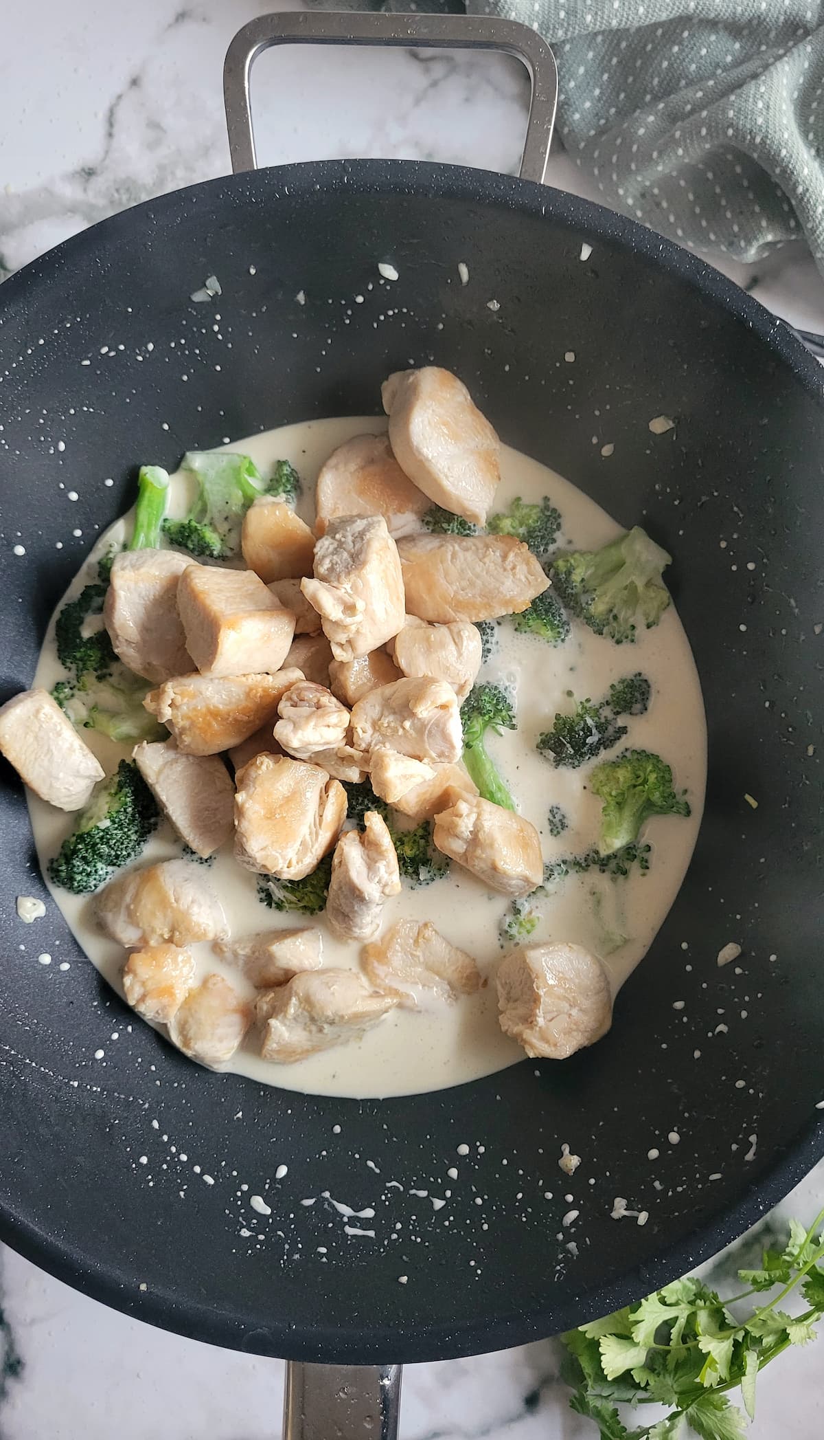 cubed chicken and broccoli florets in a creamy sauce in a wok