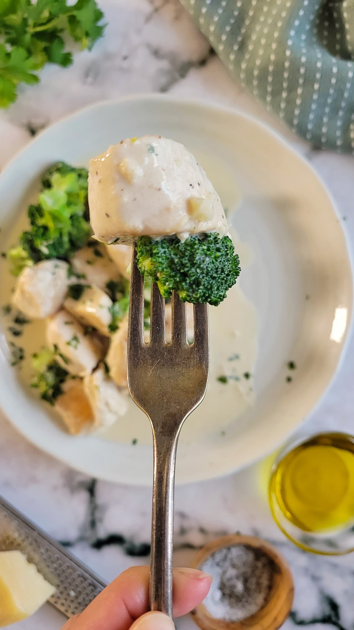 fork with a piece of chicken and broccoli over a plate with the rest