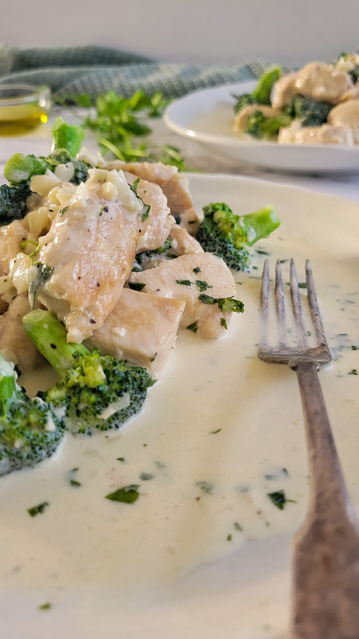 side view of a plate of chicken and broccoli with alfredo sauce, another plate in the background