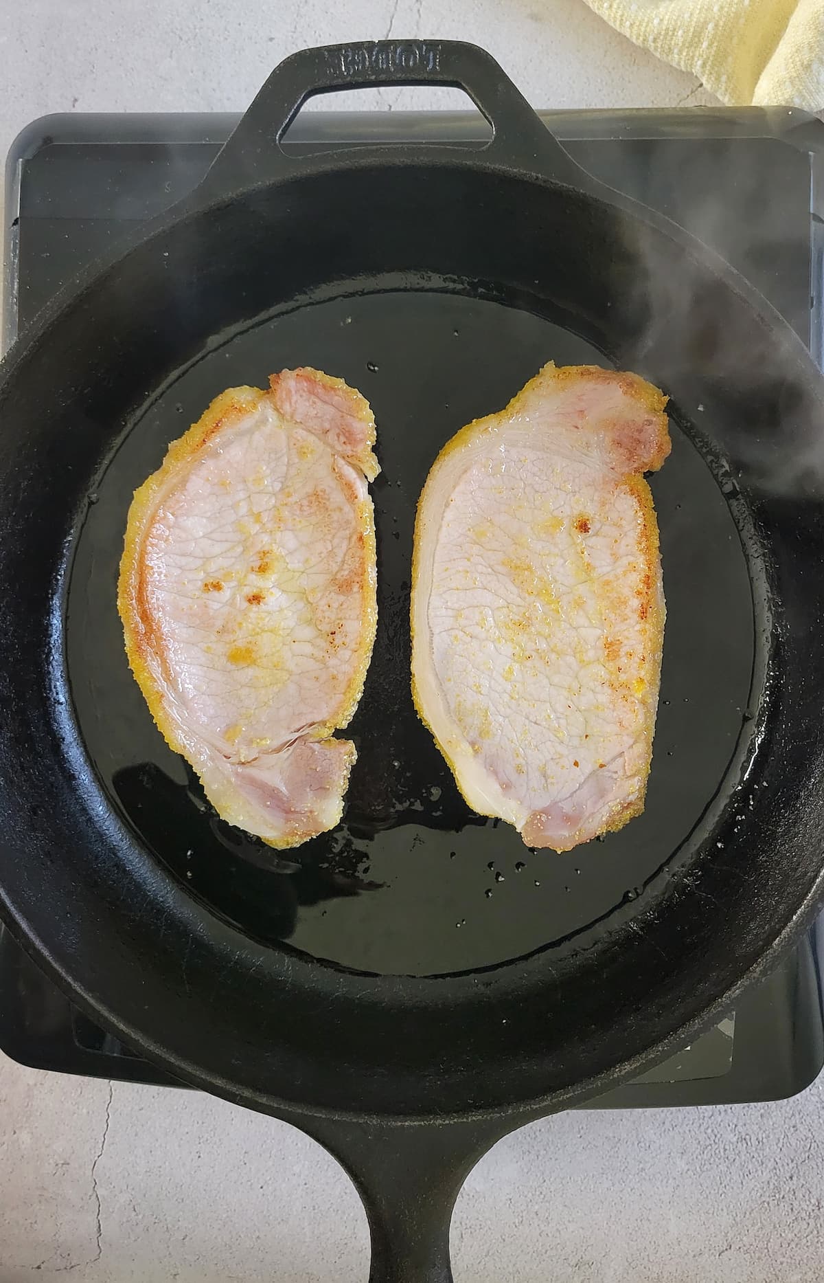2 slices of peameal bacon cooking in a cast iron skillet