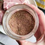 hand holding a jar of pork chop seasoning over a plate of raw pork chops