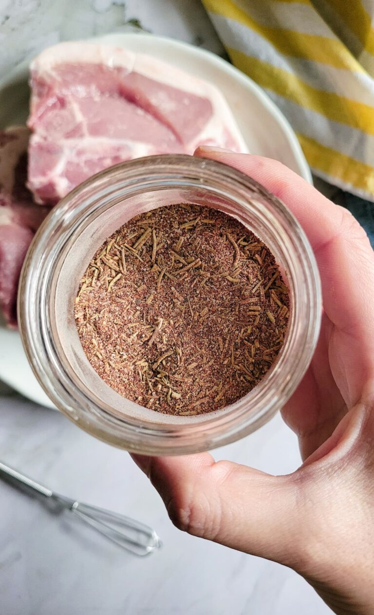 hand holding a jar of pork chop seasoning over a plate of raw pork chops