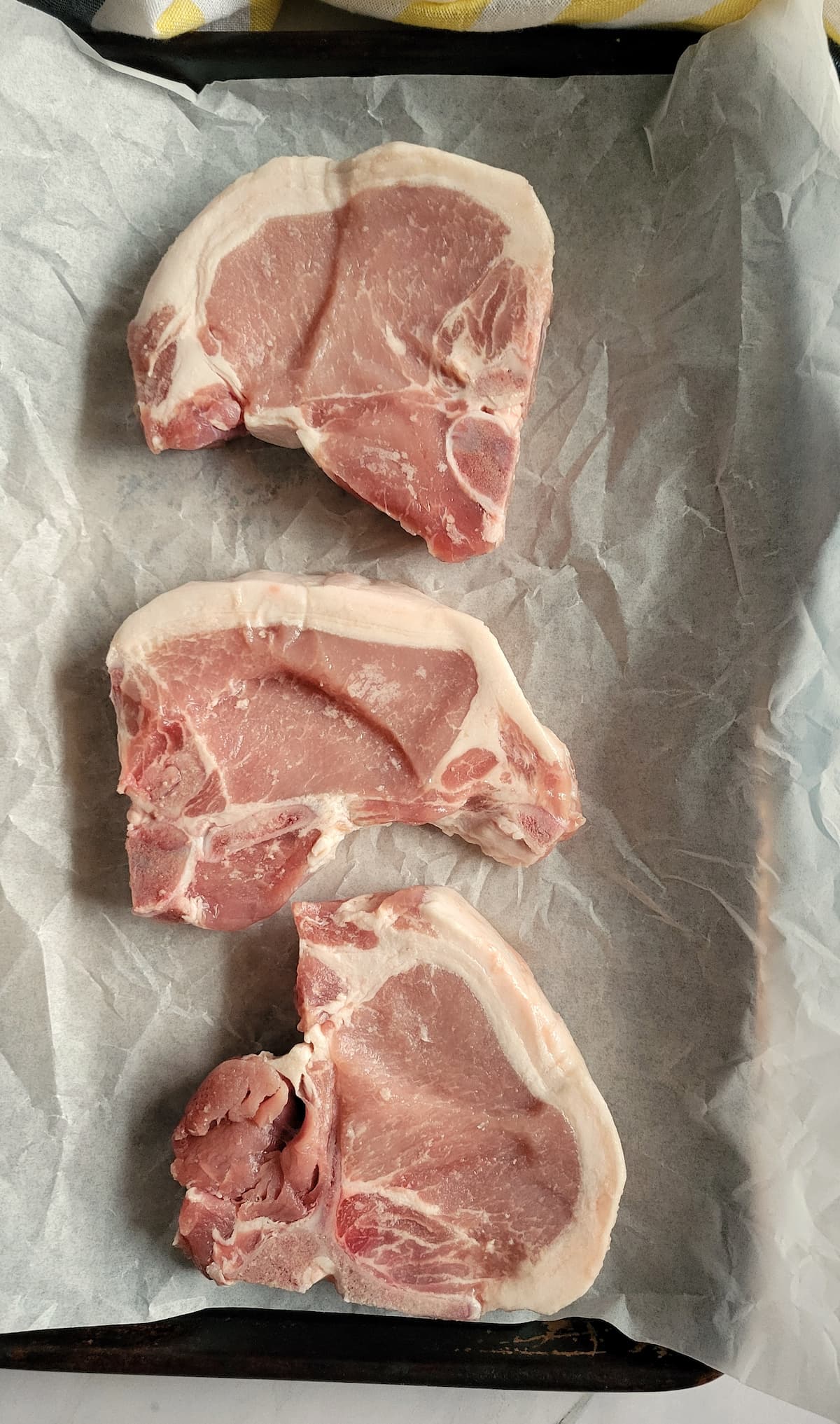 3 raw pork chops on a parchment lined baking sheet
