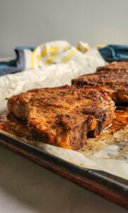 side view of cooked pork chops on a parchment lined baking sheet