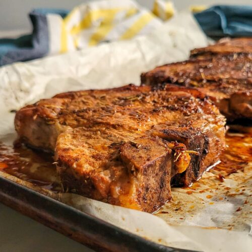 side view of cooked pork chops on a parchment lined baking sheet