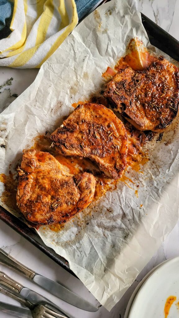 3 cooked and juicy pork chops on a parchment lined baking sheet