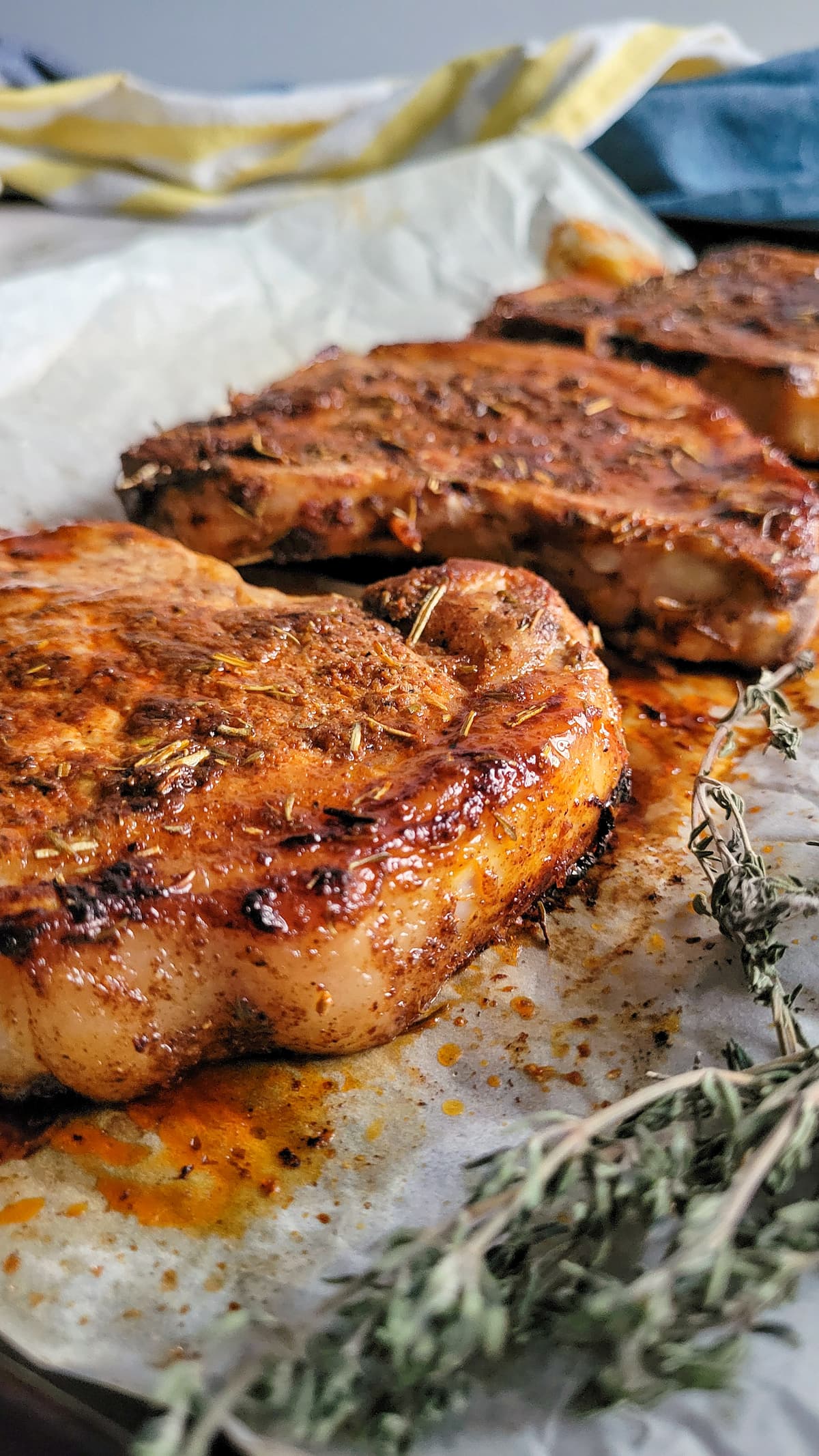 3 cooked and juicy pork chops on a parchment lined baking sheet with herbs