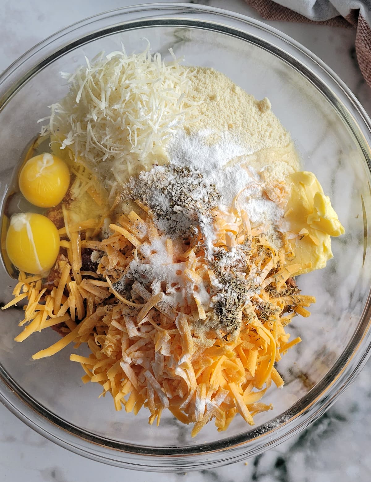 grated cheddar cheese, parmesan cheese, butter, eggs and spices unmixed in a bowl