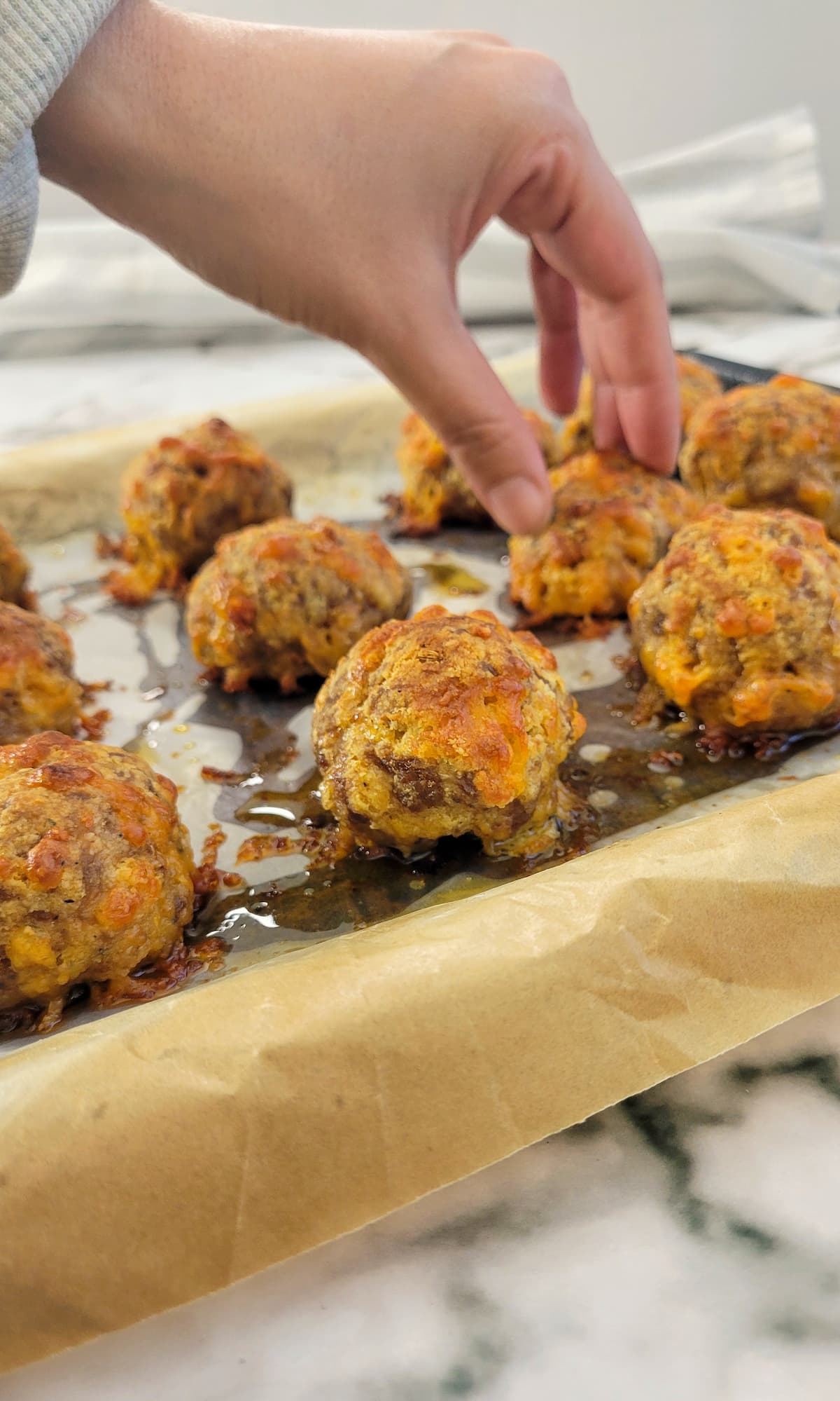 hand picking up a cooked sausage ball off a parchment lined baking sheet with more