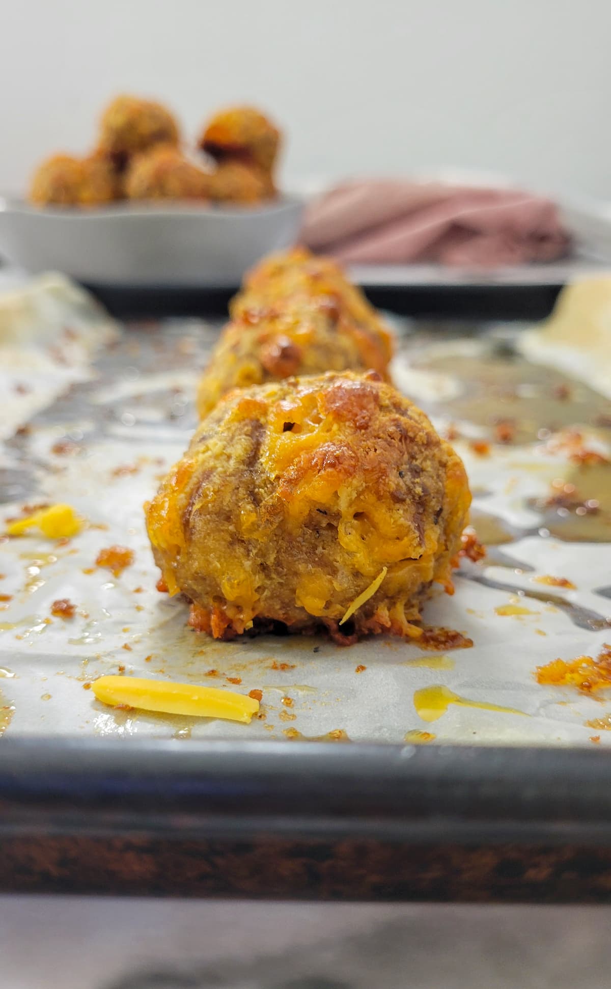 cooked sausage balls on a parchment lined baking sheet, bowl with more in the background