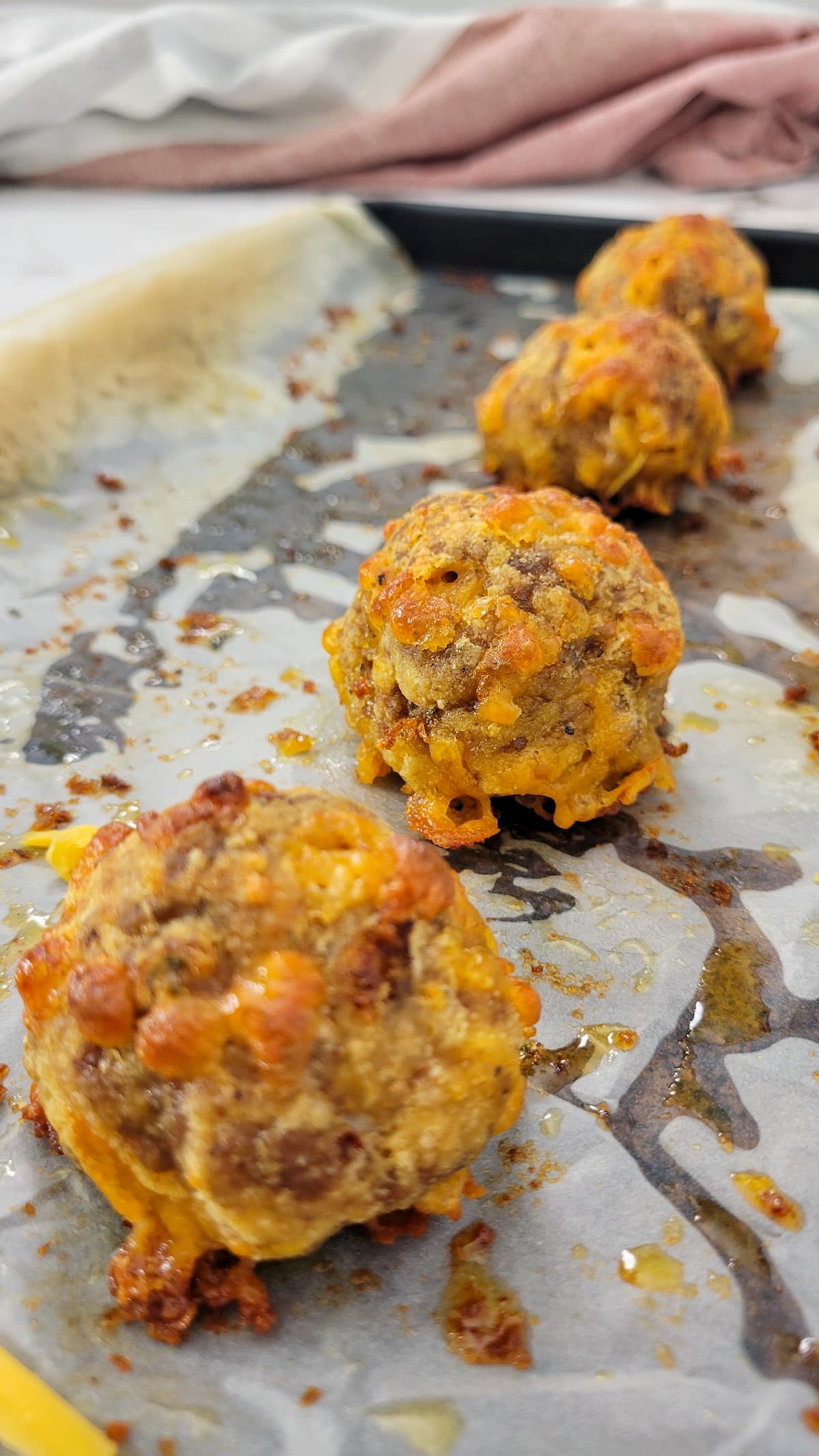 4 cooked sausage balls on a parchment lined baking sheet