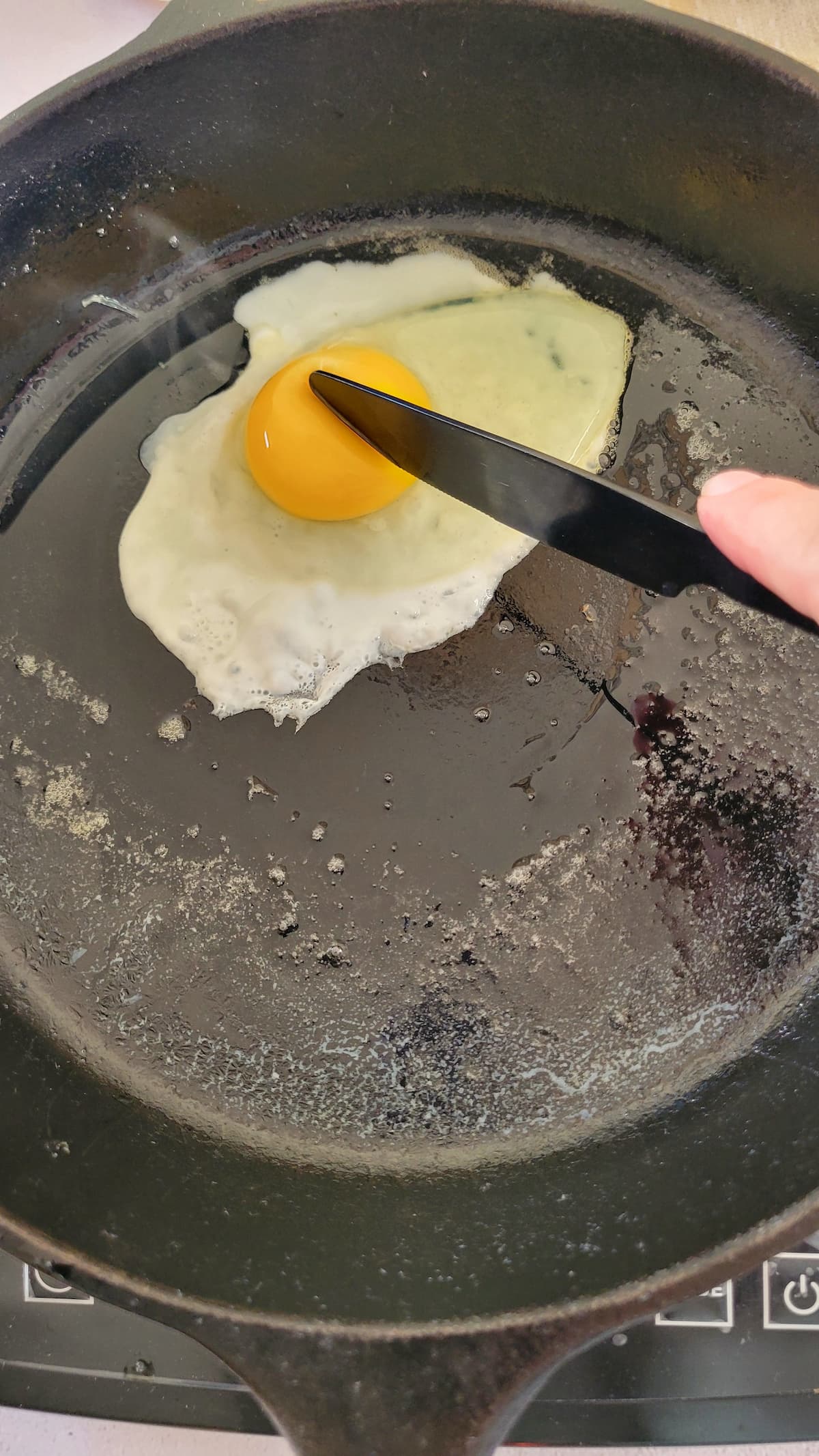egg in a cast iron skillet with a knife breaking the yolk