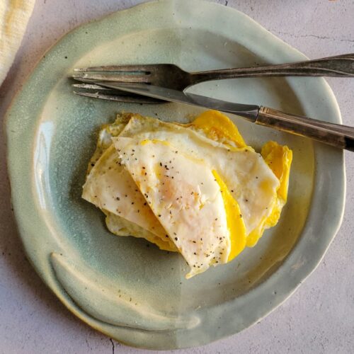 over hard eggs on a plate with a fork and knife, bacon in the background