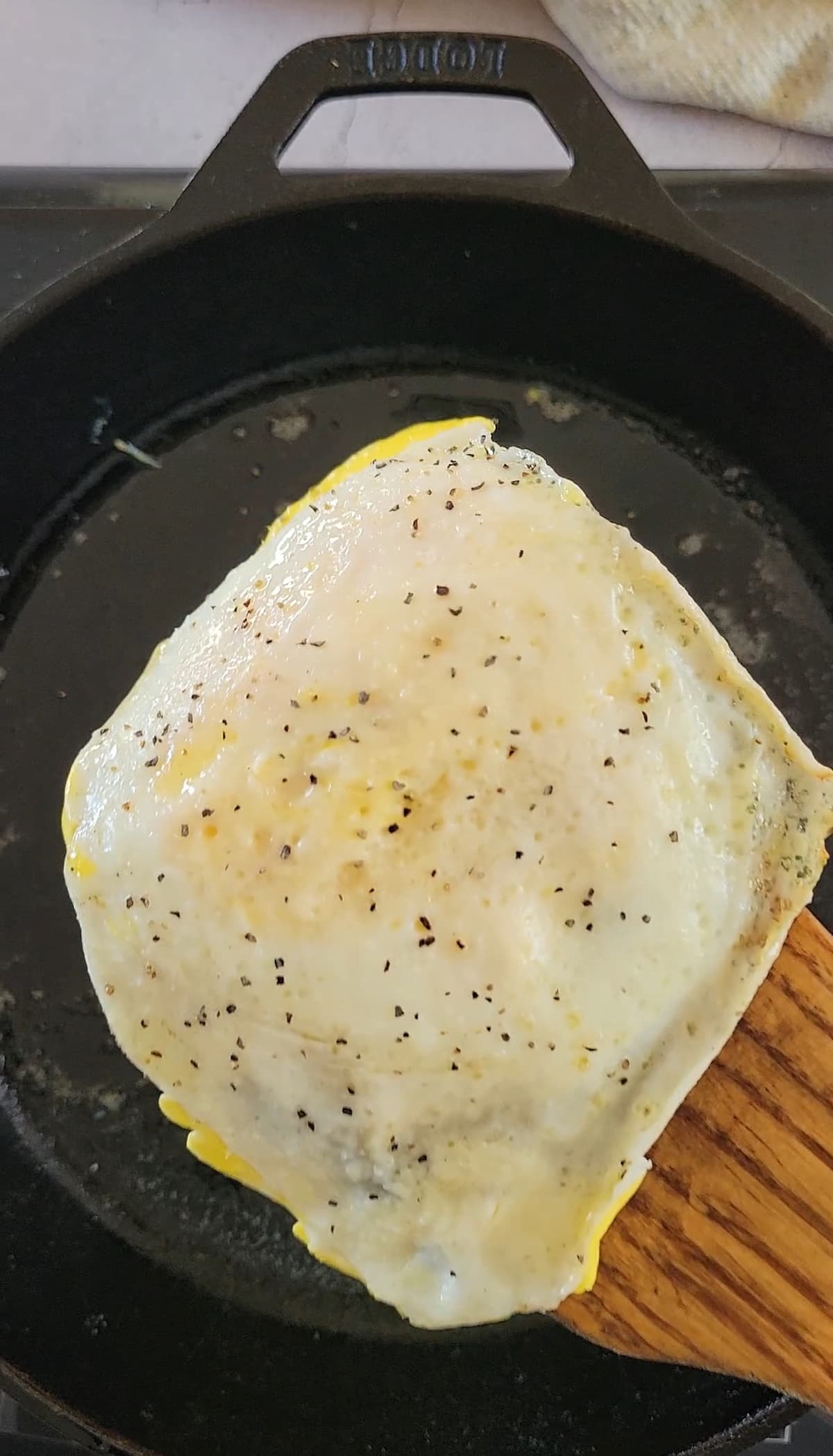 over hard fried egg with salt and pepper on a spatula over a cast iron skillet