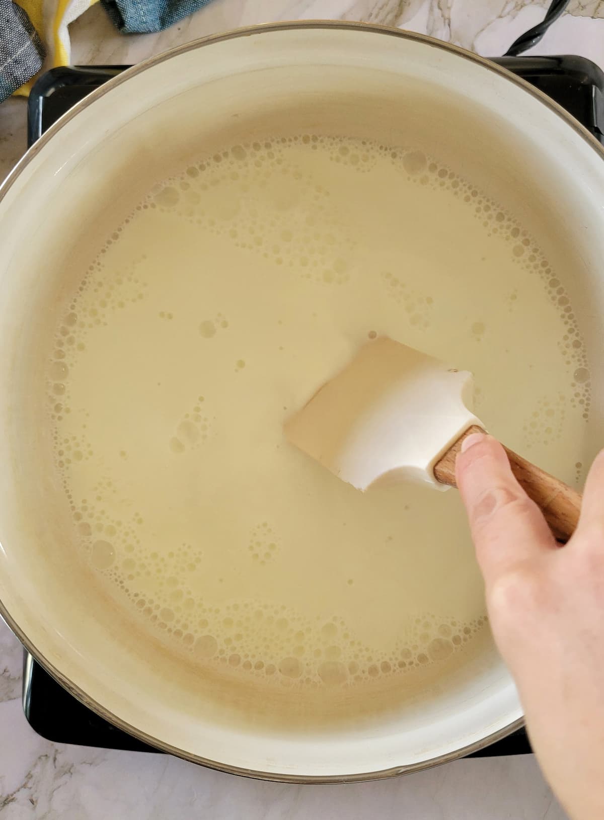 hand with a rubber spatula stirring milk in a pot