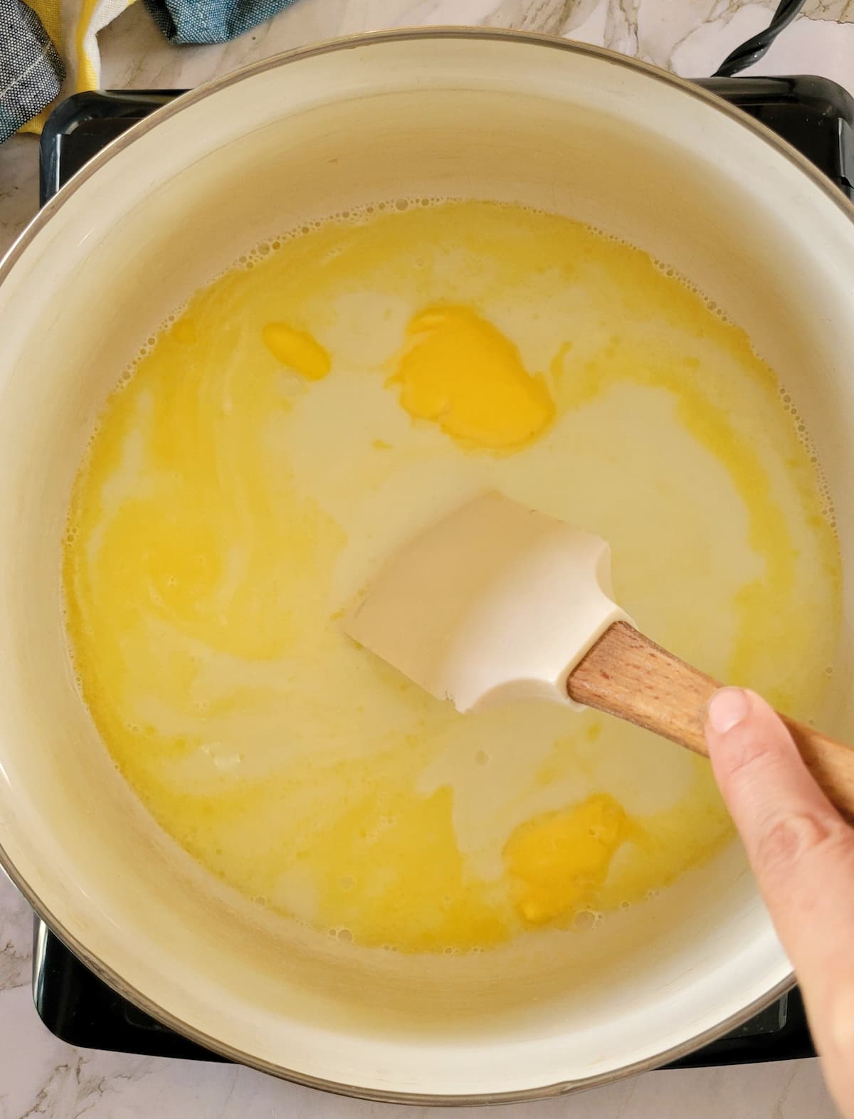 hand with a rubber spatula stirring butter into milk in a pot