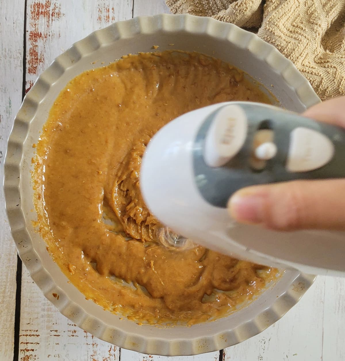 hand with a blender blending caramel sauce in a pan