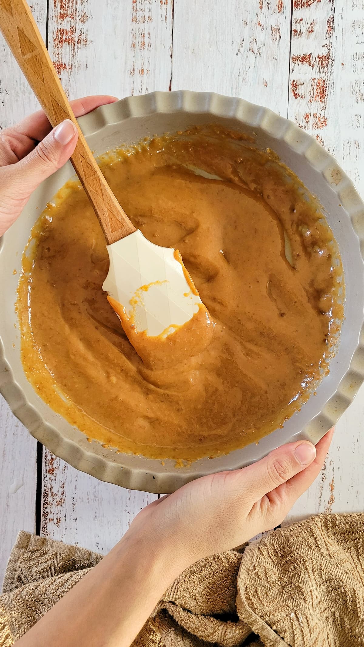hands holding a dish with homemade caramel sauce and a rubber spatula