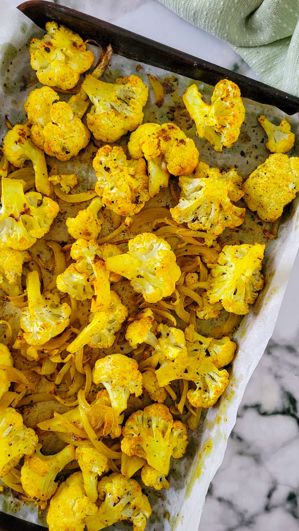 baked yellow cauliflower and onions on a parchment lined baking sheet