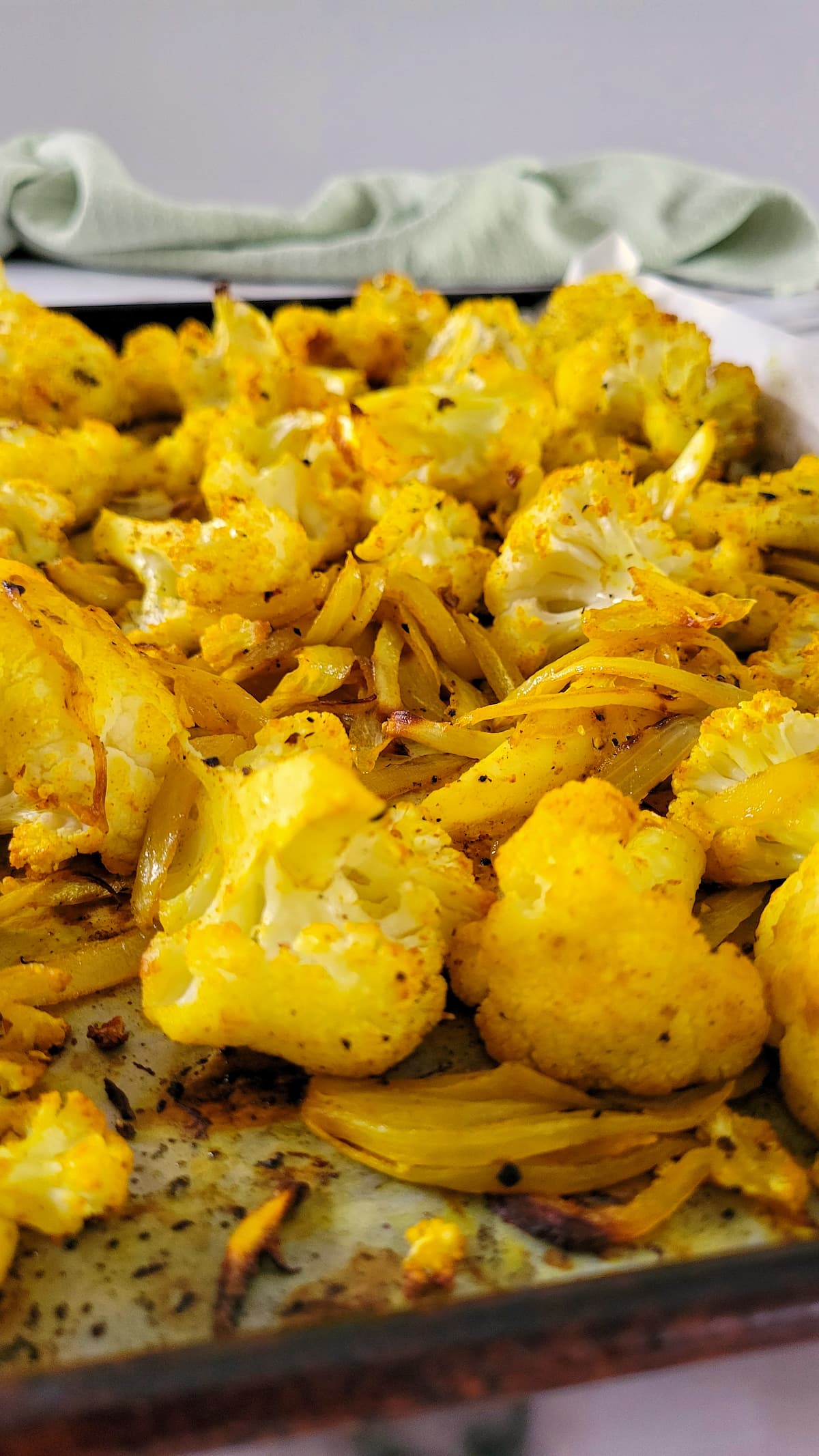 side view of yellow cauliflower and onions on a parchment lined baking sheet