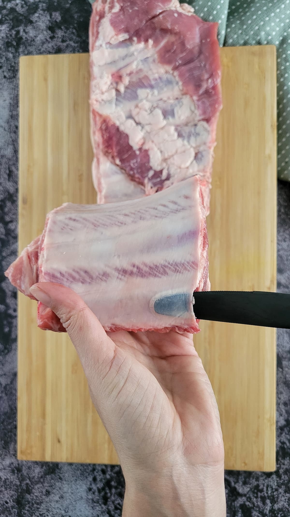 knife underneath the membrane of a raw rack of ribs