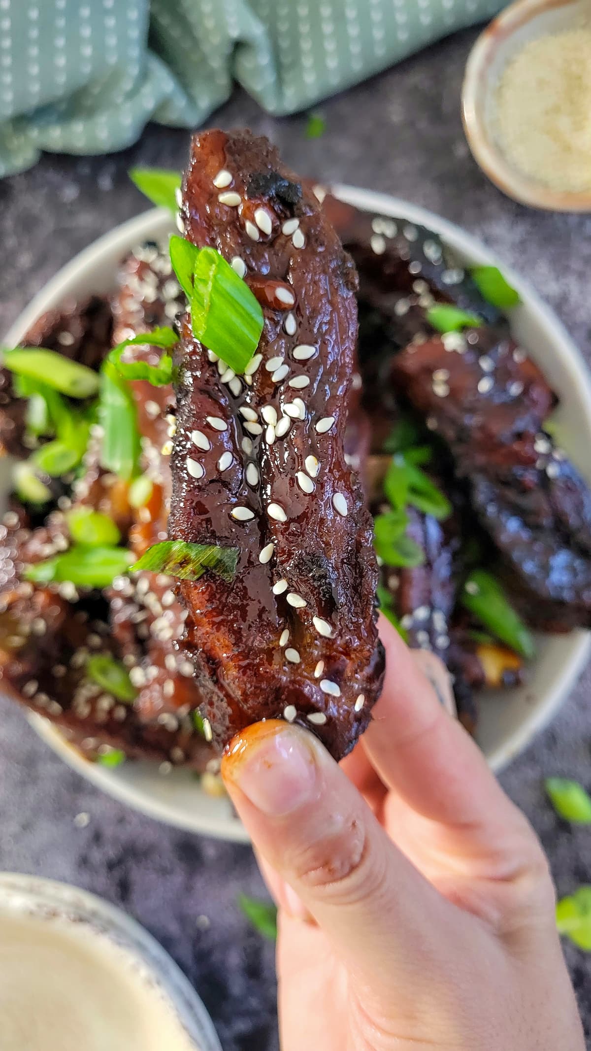 hand holding a rib with sesame seeds and green onions over a bowl with more