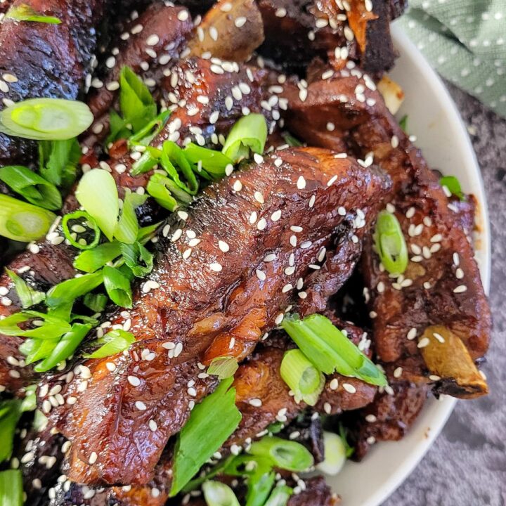 bowl of sticky asian ribs with green onions and sesame seeds