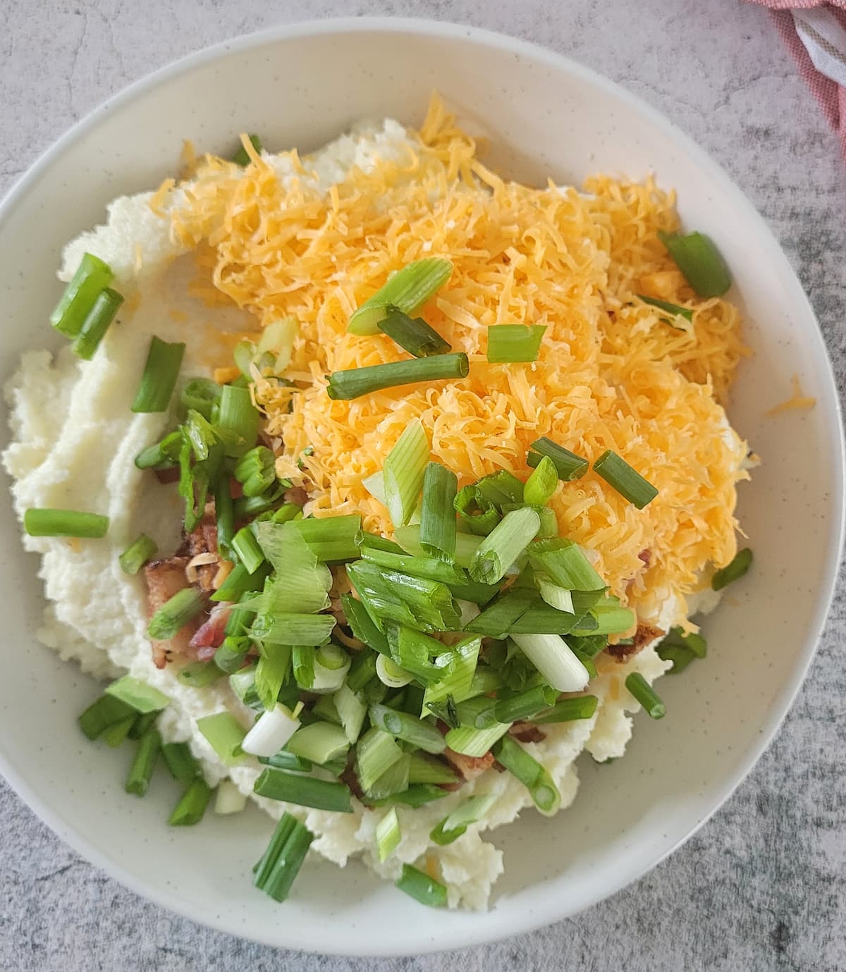 chopped green onions, shredded cheddar, bacon bits on top of a pile of mashed cauliflower