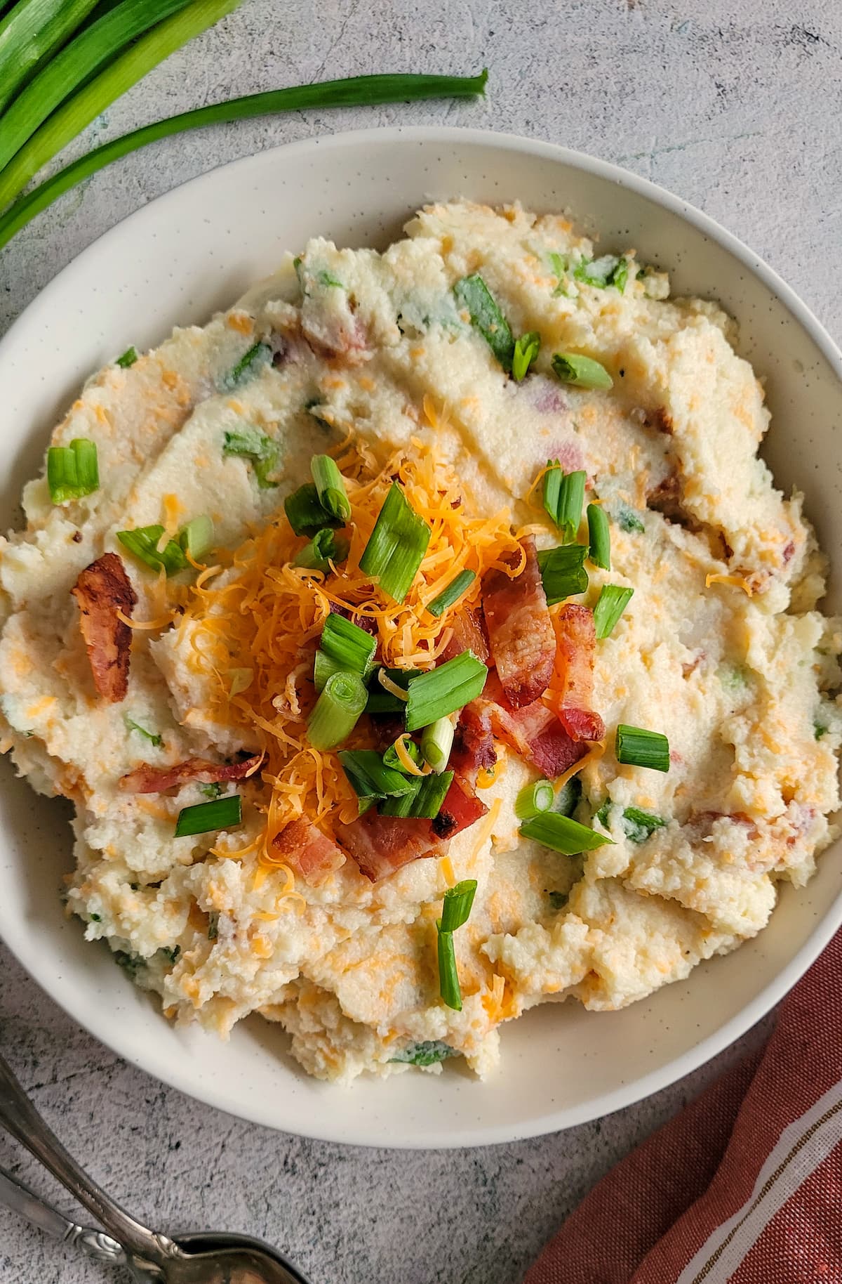 loaded mashed cauliflower in a bowl topped with green onions, cheddar cheese and bacon
