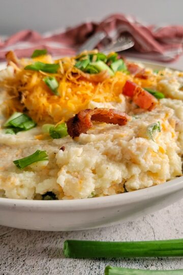 mashed cauliflower in a bowl topped with bacon, green onions and cheddar cheese